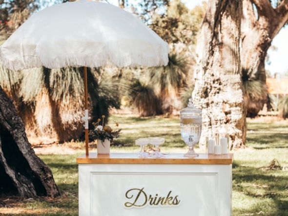 White drinks cart with fringed umbrella, glass dispensers and champagne