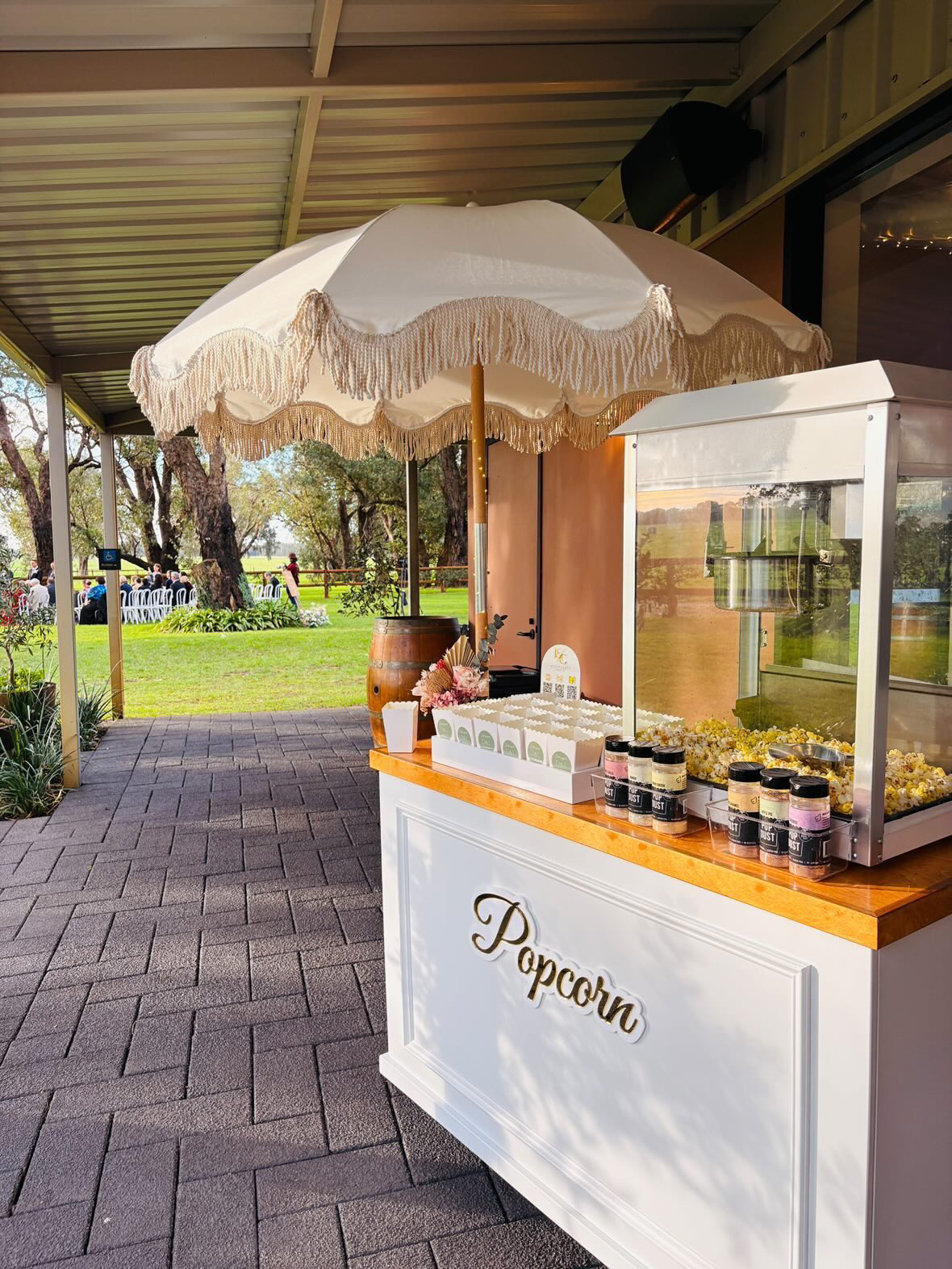 White popcorn cart with fringed parasol and popcorn machine at an outdoor wedding